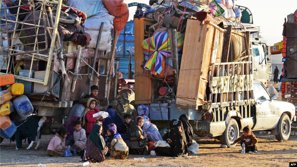 Afghan refugees along with their belongings sit beside the trucks at a registration center, upon their arrival from Pakistan in Takhta Pul district of Kandahar province on December 18, 2023. (Photo by Sanaullah SEIAM / AFP)