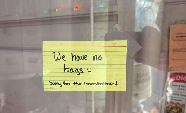 A yellow index card taped to a window that reads "We Have No Bags :( Sorry for the inconvenience."