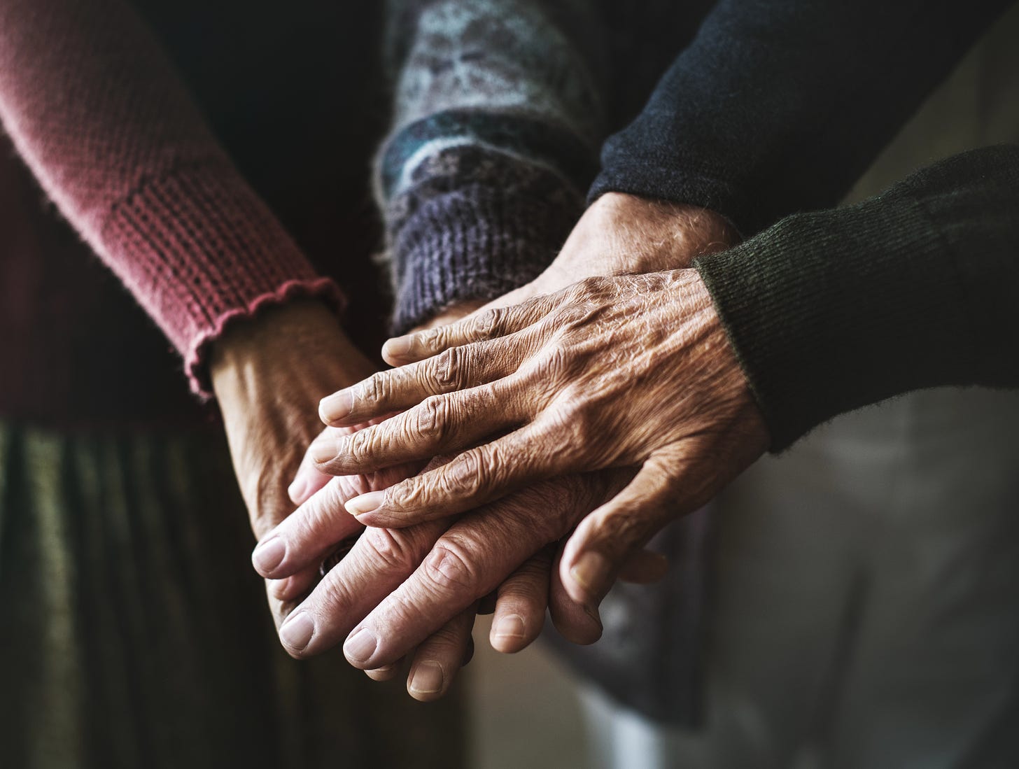 Close-up of several mature hands stacked on top of one another