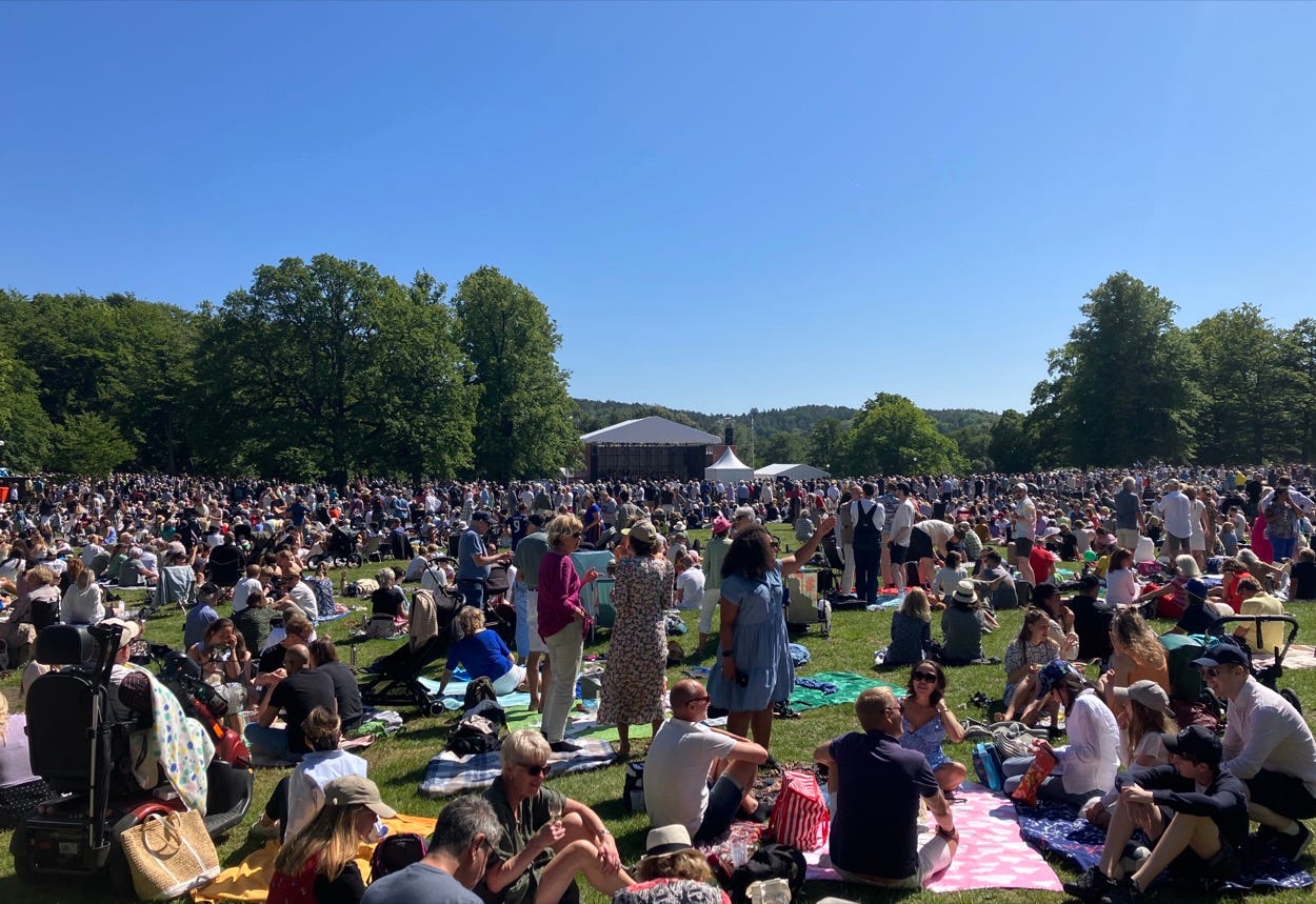 Large crowd sitting on the grass in front of a stage