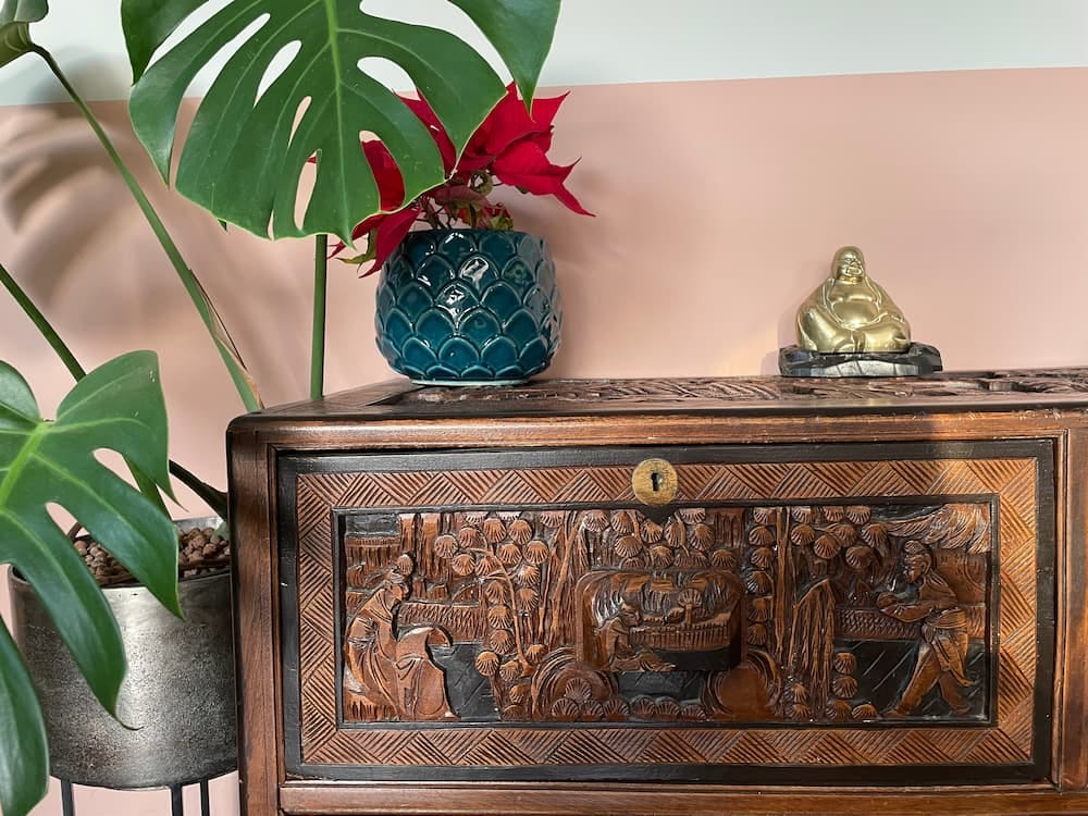 Photo of the top left of the chinese chest with a house plant to the left and a brass Buddha on top