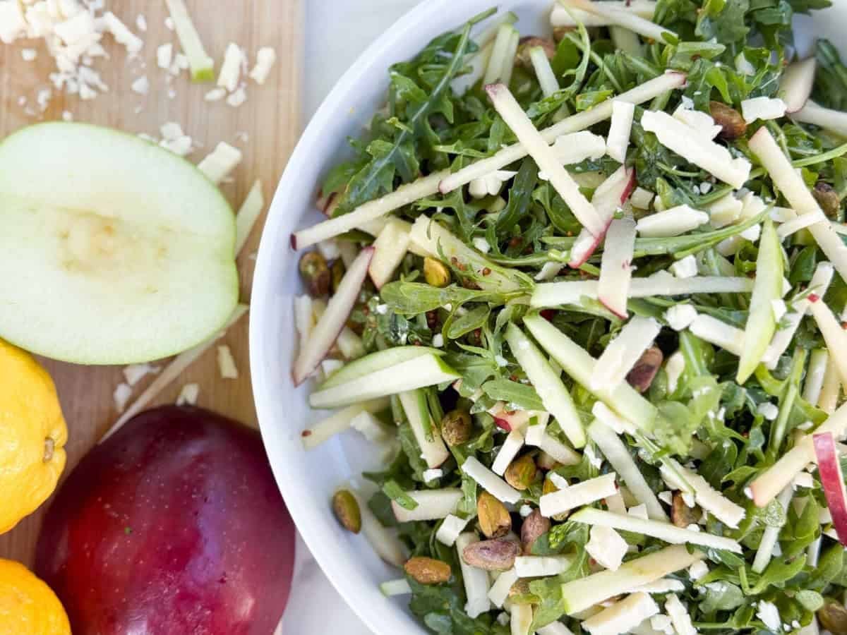 a bowl of arugula, apples, cheese and pistachio salad