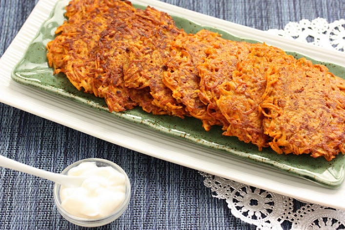 A long plate of 6 overlapped latkes, with a bowl of sour cream nearby.