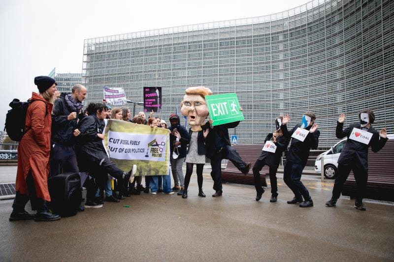 Protestors at Schuman roundabout holding signs that say 'Cut fossil fuels out of our politics' while some are dressed as politicians with gas and oil lobbyists