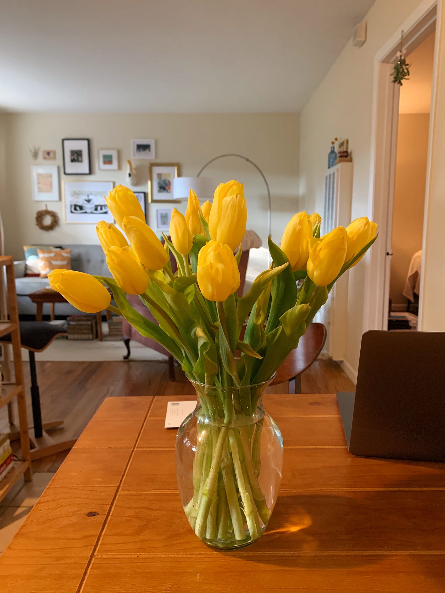 A bright yellow bouquet in a vase sits on a wooden table.