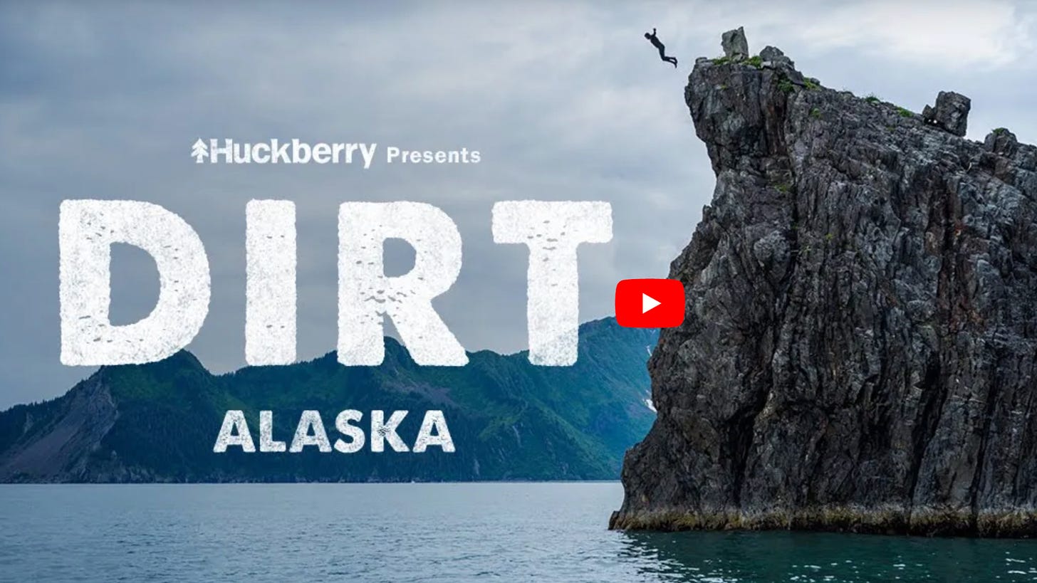 The YouTube thumbnail for DIRT Alaska where a guy is jumping off a giant rock into clear blue water. 