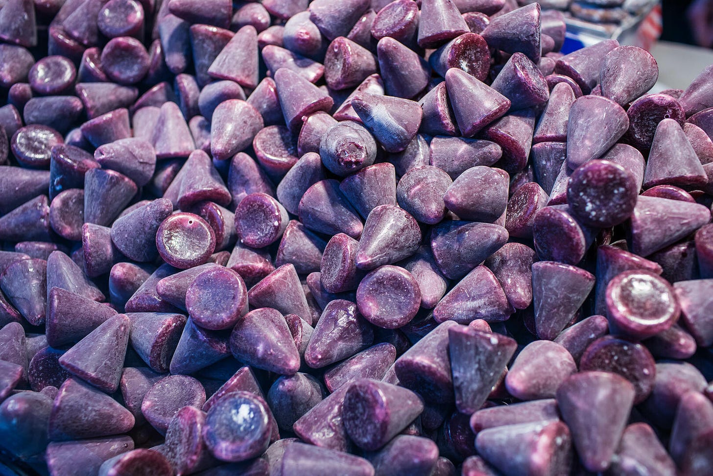 Een foto gevuld met tientallen cuberdons: kegelvormige, paarse snoepjes.