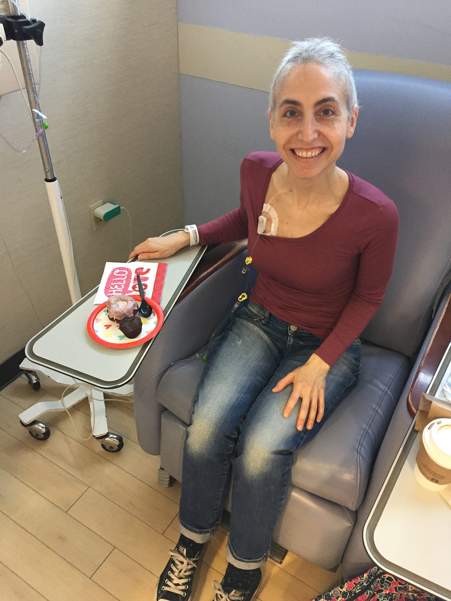 Me at chemo on Valentine's Day, sitting in the chair getting my infusion, with a plate of baked goods on the arm rest in front of me