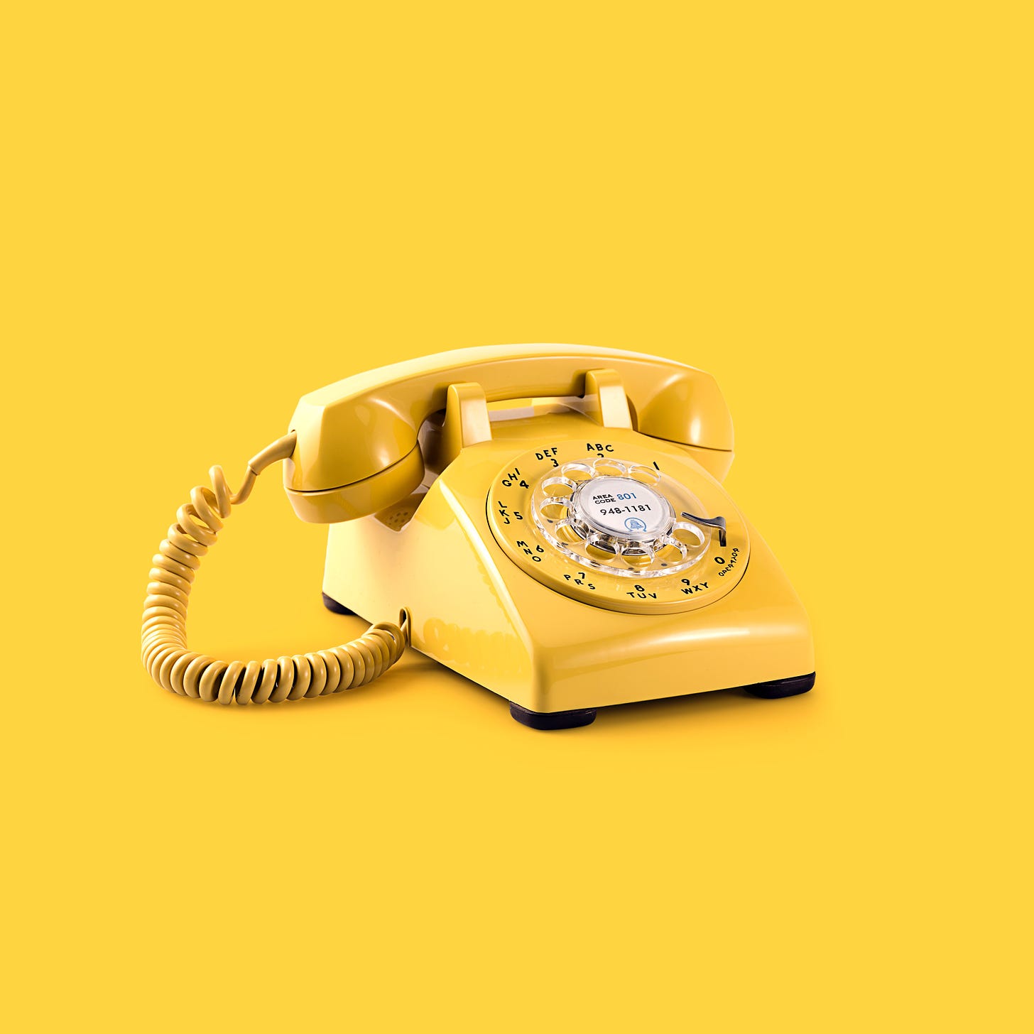 A yellow rotary phone with a yellow background.