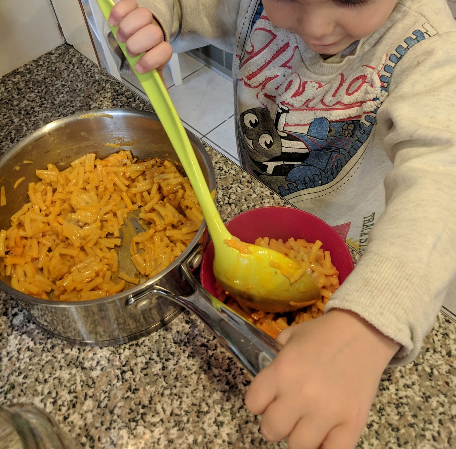 A little boy smiles as he stirs a pot of instant mac and cheese