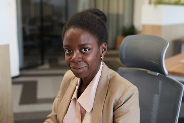 Black woman wearing beige and pink business suit, seated, looking directly at camera