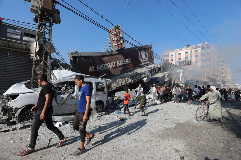 People walk past the wreckage of a bakery and a car People walk past the wreckage of a bakery and a car