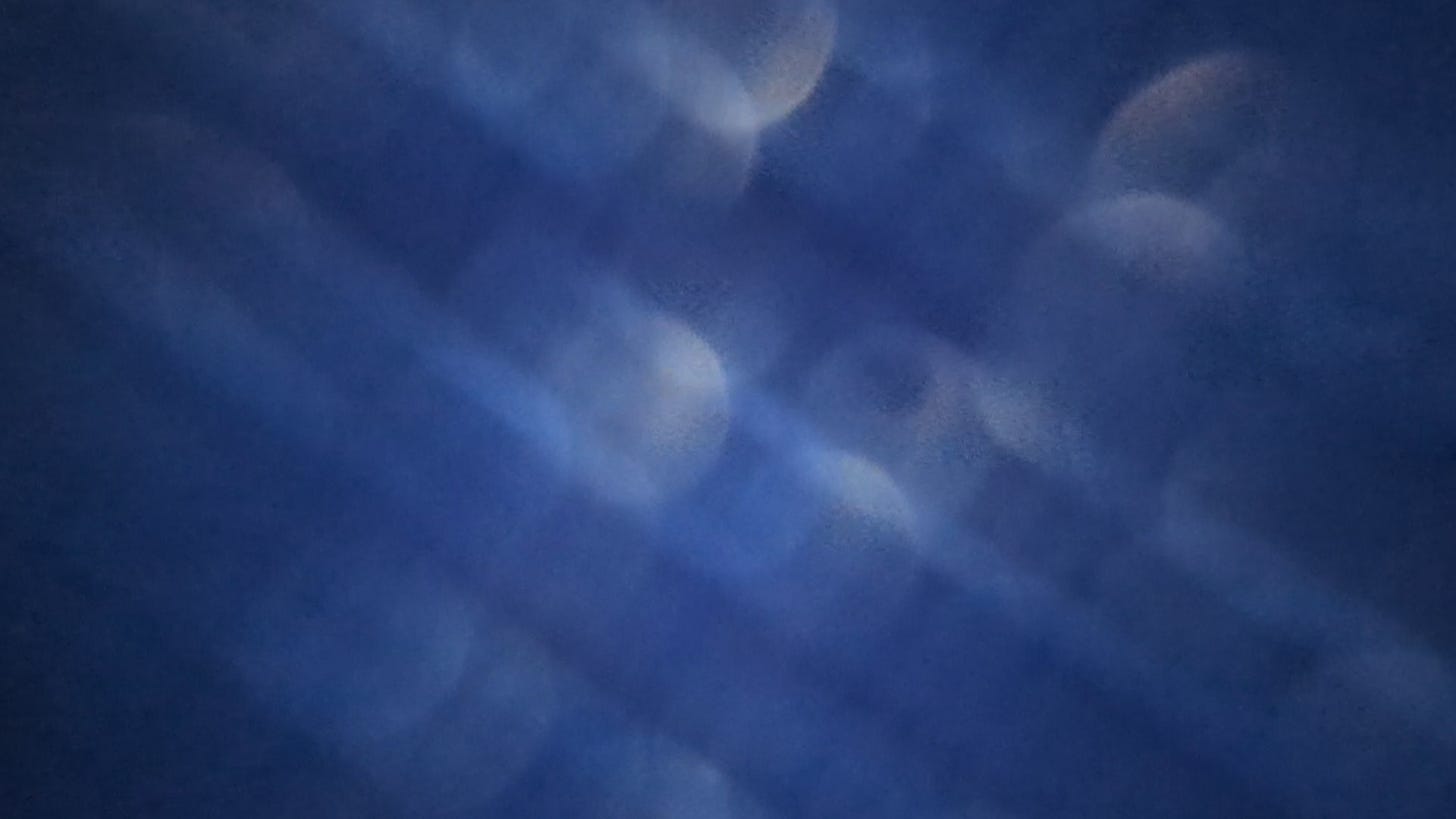 A closeup photo through blue fabric shows diagonal streaks of different shades of blues with translucent white circles of light layered throughout
