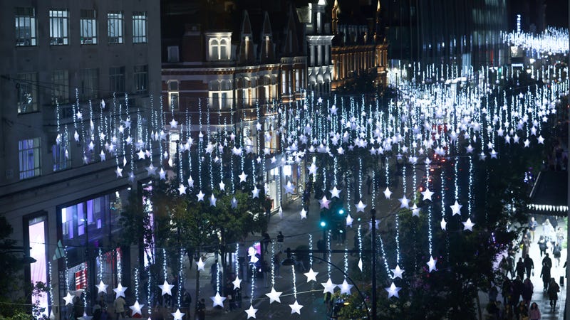 Hundreds of bright blue LED stars hang from garlands above Regent Street at night time with shops lining the street and people walking beneath