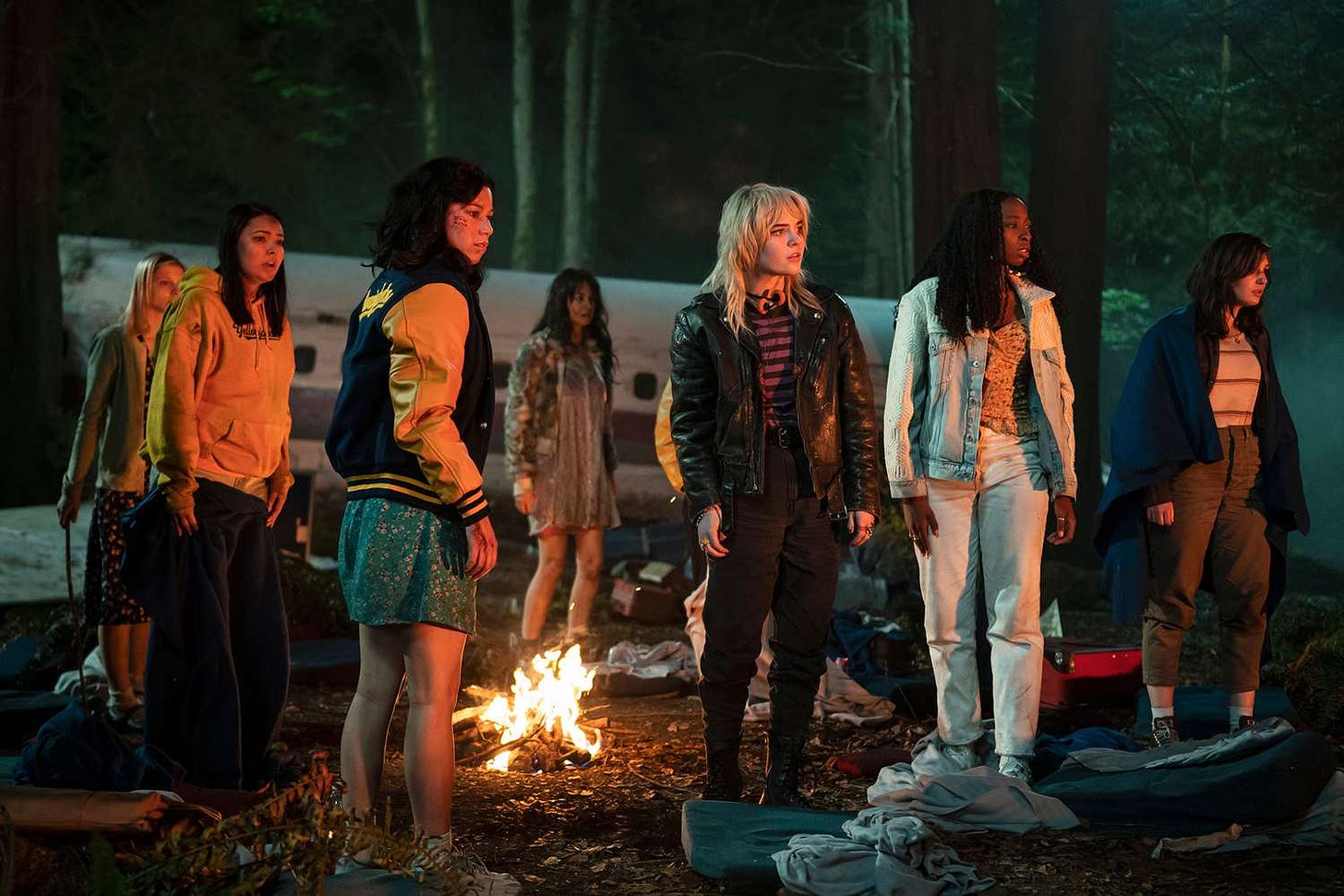 The Yellowjackets around a fire, gazing off to screen right.
