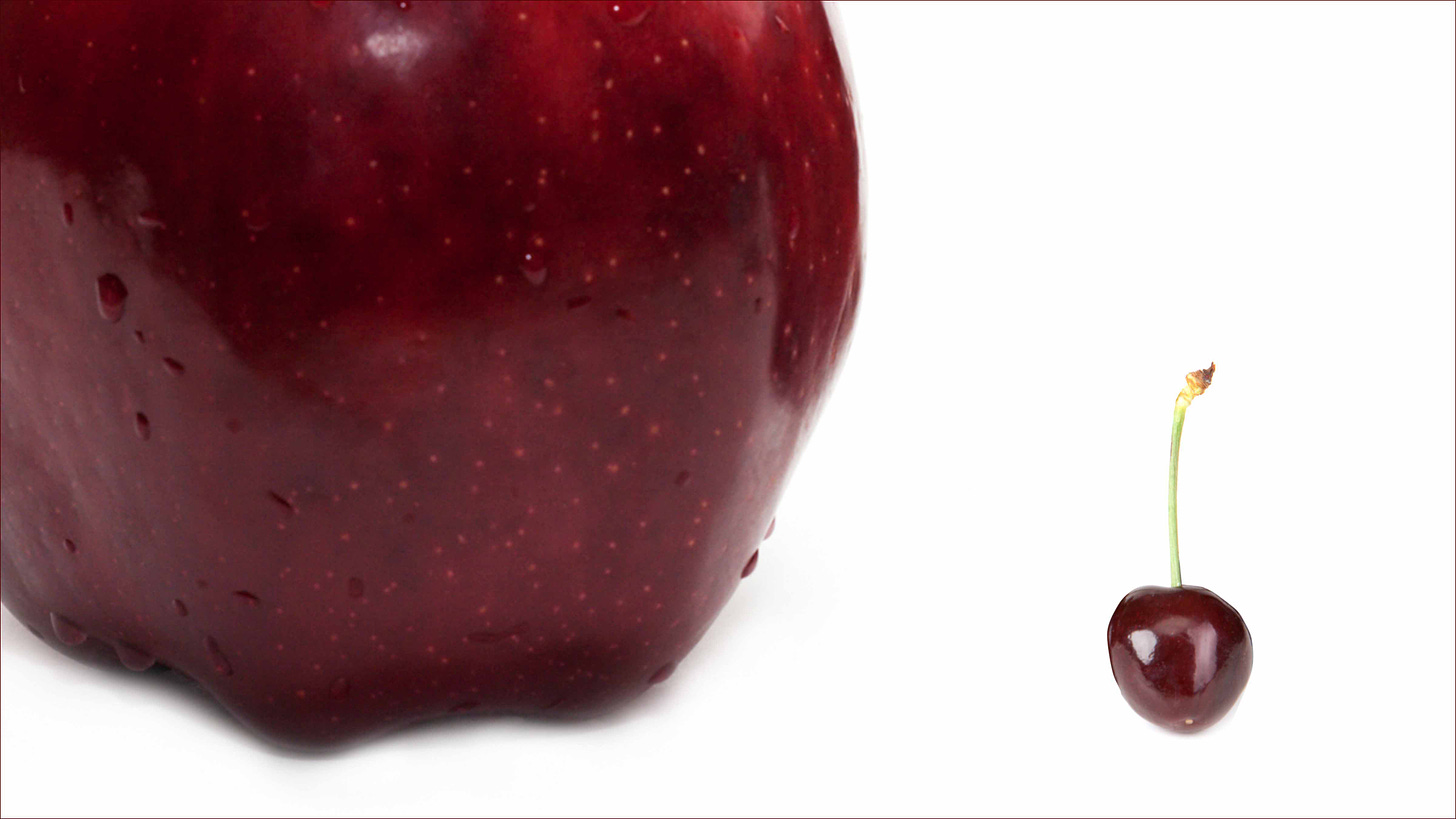 A great big apple next to a cherry