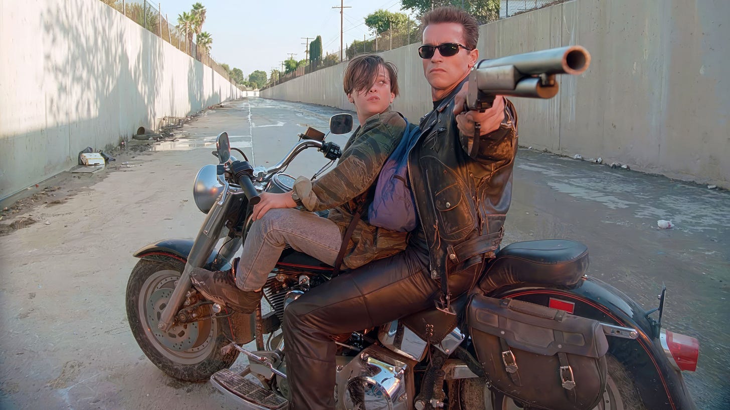 Terminator 2: Judgment Day | Still features Edward Furlong on a bike together with Arnold Schwarzenegger as the T-800, wielding a shotgun.