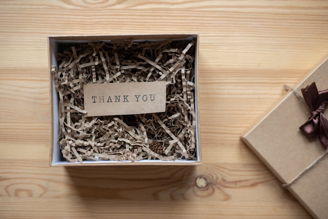 Free Top view of opened carton present box with small postcard with Thank You inscription and paper stuffing on wooden table Stock Photo