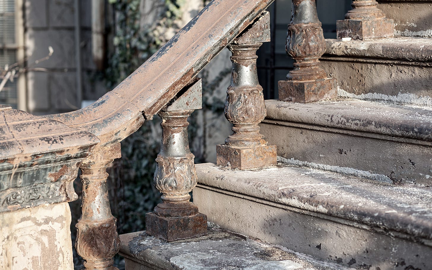 Old brownstone steps with ancient railing. The sun burns away the rust and grime.