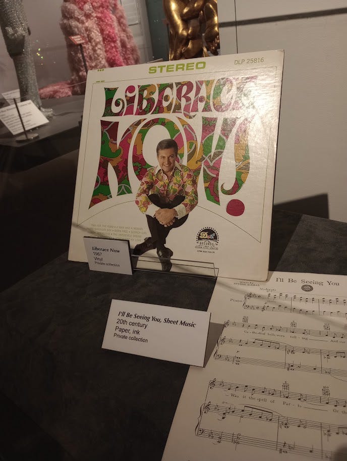 LP record album called Liberace Now! with Liberace in colorful late 1960s attire, sheet music, and outrageous Liberace outfits in background