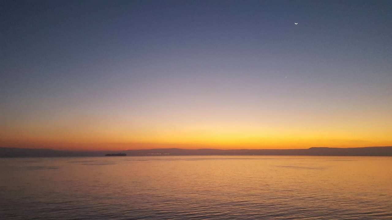 a sunset over the ocean with a crescent moon in the sky