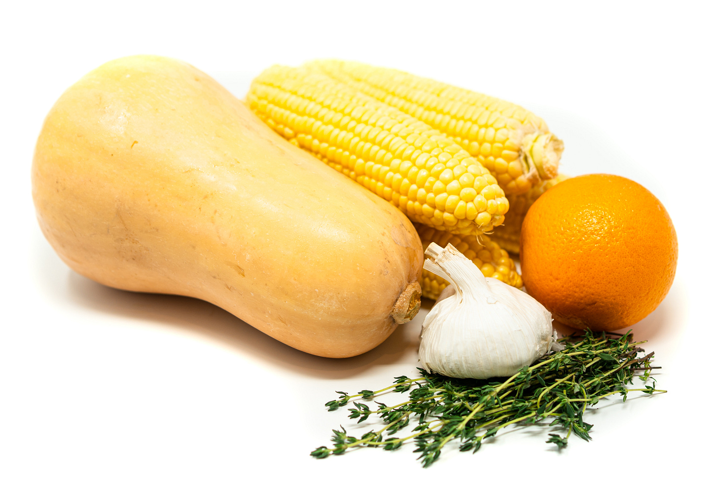 Fresh whole ingredients including butternut squash, corn on the cob, garlic, orange, and thyme arranged on a white background. Fresh whole ingredients including butternut squash, corn on the cob, garlic, orange, and thyme arranged on a white background.