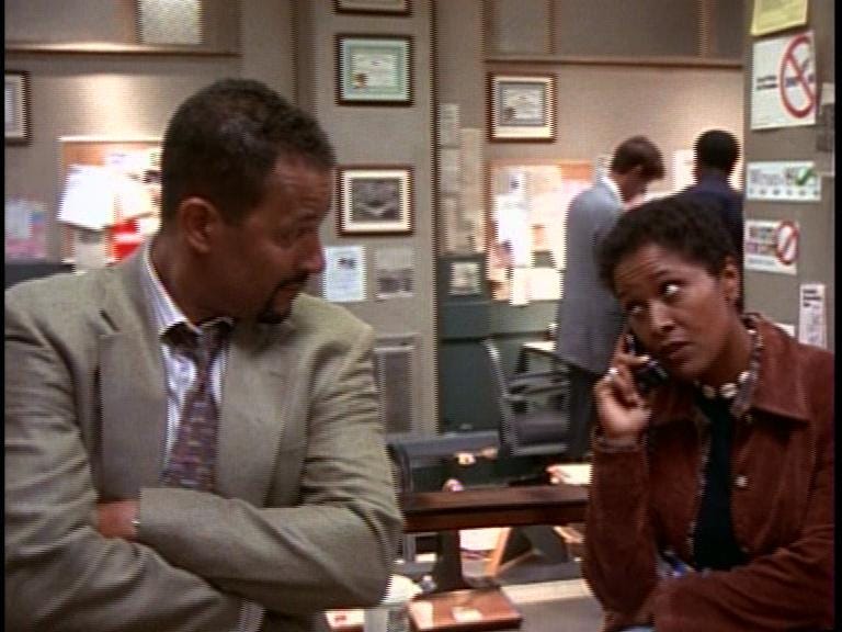 This still image from "Bad Medicine," the fourth episode of Homicide: Life on the Street's fifth season, shows Detective Meldrick Lewis (played by Clark Johnson, left) listening as Detective Terri Stivers (played by Toni Lewis, right) speaks via telephone with a suspect they wish to interrogate. Lewis and Stivers lean against a desk in the Baltimore Homicide Unit's squad room. This still image from "Bad Medicine," the fourth episode of Homicide: Life on the Street's fifth season, shows Detective Meldrick Lewis (played by Clark Johnson, left) listening as Detective Terri Stivers (played by Toni Lewis, right) speaks via telephone with a suspect they wish to interrogate. Lewis and Stivers lean against a desk in the Baltimore Homicide Unit's squad room.