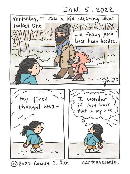 Pink Bear Head Hoodie 3-panel autobio comic of a girl with a braid walking in Central Park in winter. She passes a kid who is holding hands with an adult and wearing a pink bear head hoodie with a bear nose and ears, which make it look like the kid's head is in the bear's mouth. Caption reads, "Yesterday, I saw a kid wearing what looked like a fuzzy, pink bear head hoodie." In panel 2, the girl with the braid walks on. In panel 3, girl turns to look back at them. Text reads, "My first thought was -", followed by a thought bubble that says, "I wonder if they have that in my size." Original comic cartoon by Connie Sun, cartoonconnie