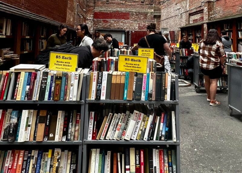 Image of outdoor bookshelf filled with books sold for five dollars. Brick wall in background.