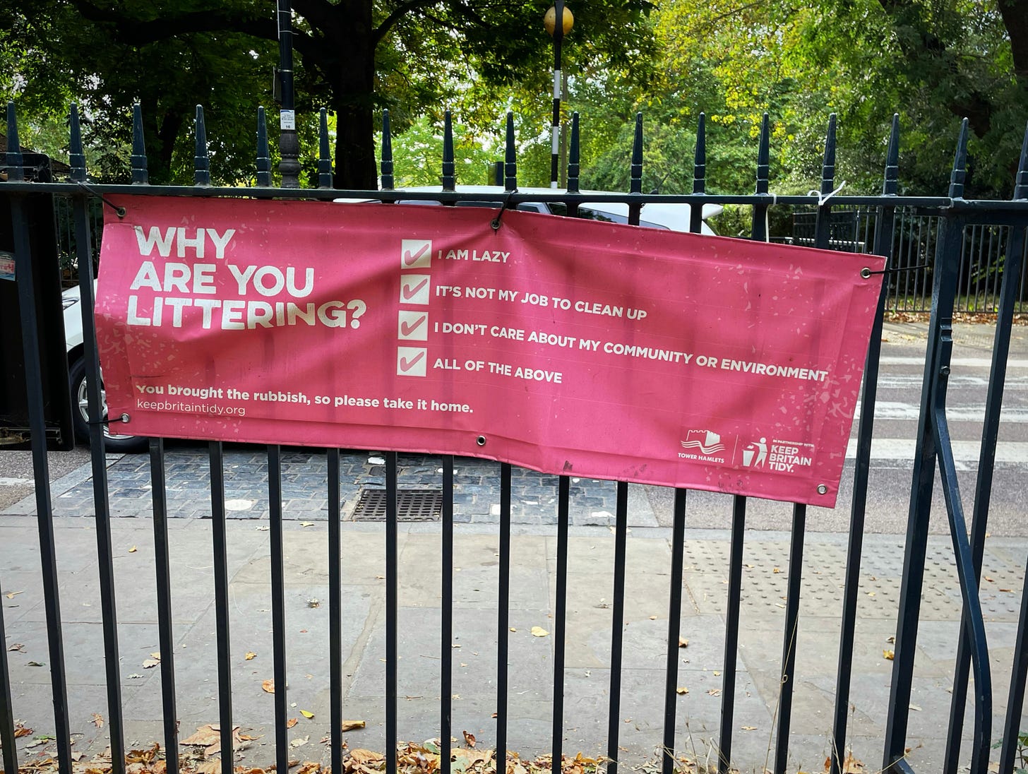 Red banner at Victoria Park London with white text that says 'Why are you littering?' and the words 'I am lazy, It's not my job to clean up, I don't care about my community or environment, all of the above