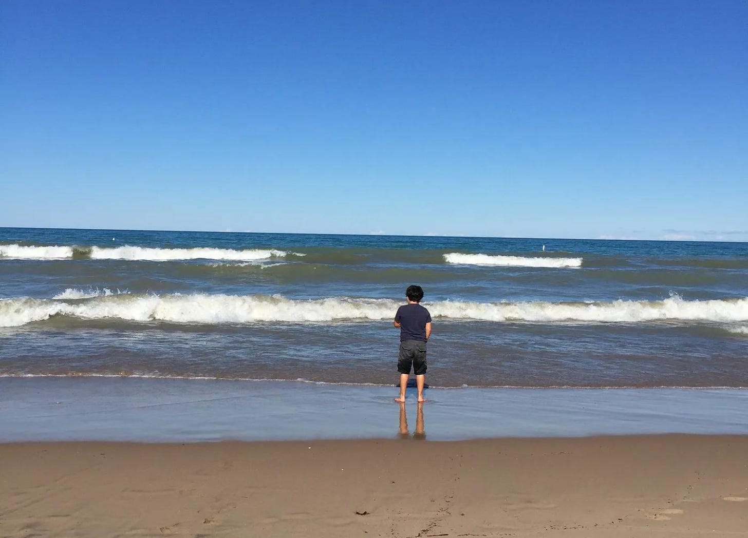 Kid standing at the shoreline with waves coming in.