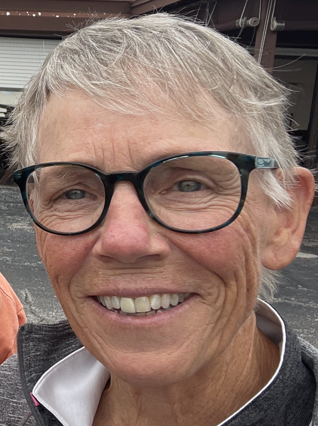 An elderly woman with short-cropped hair, glasses, and a big smile