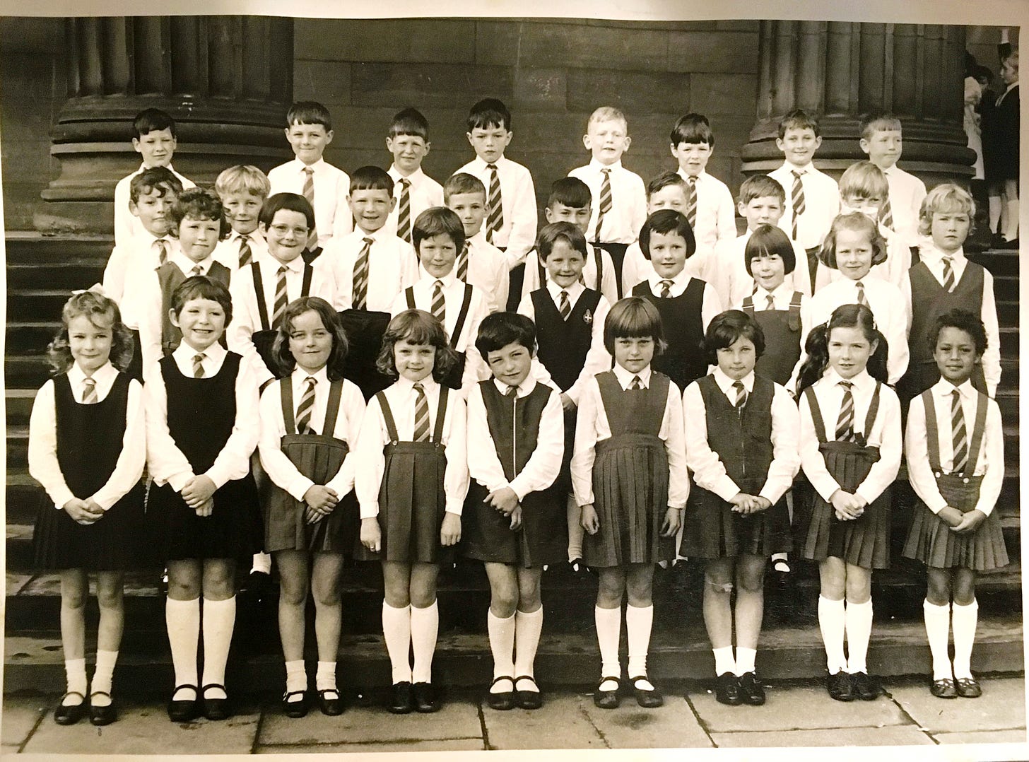 black and white photo of 4 neat rows of kids in school uniform outside a Victorian concert hall