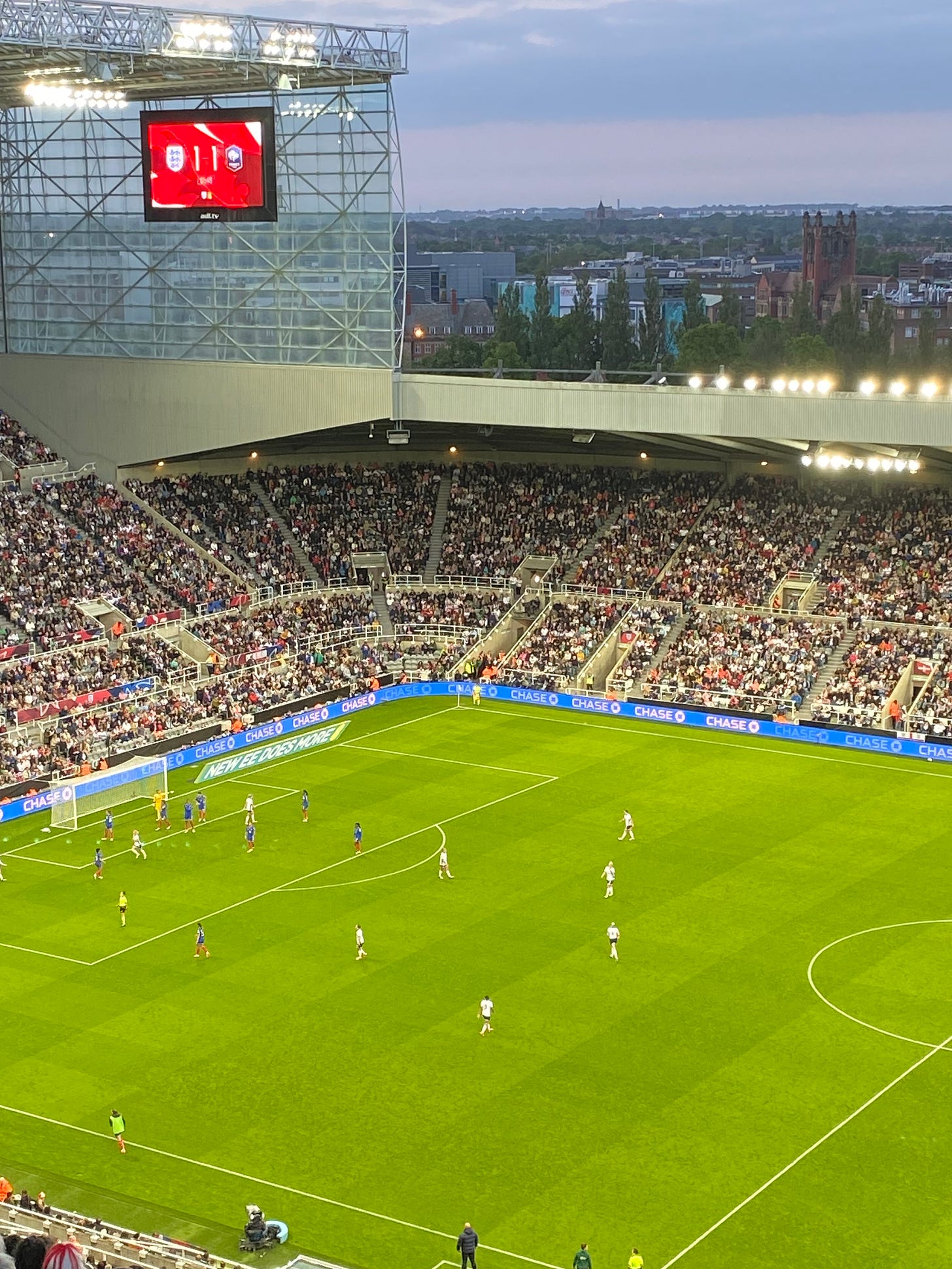 A view of the pitch at St. James' Park, the England-France game in progress, with the scoreboard behind it, reading 1-1. It's dusk and the floodlights are on.