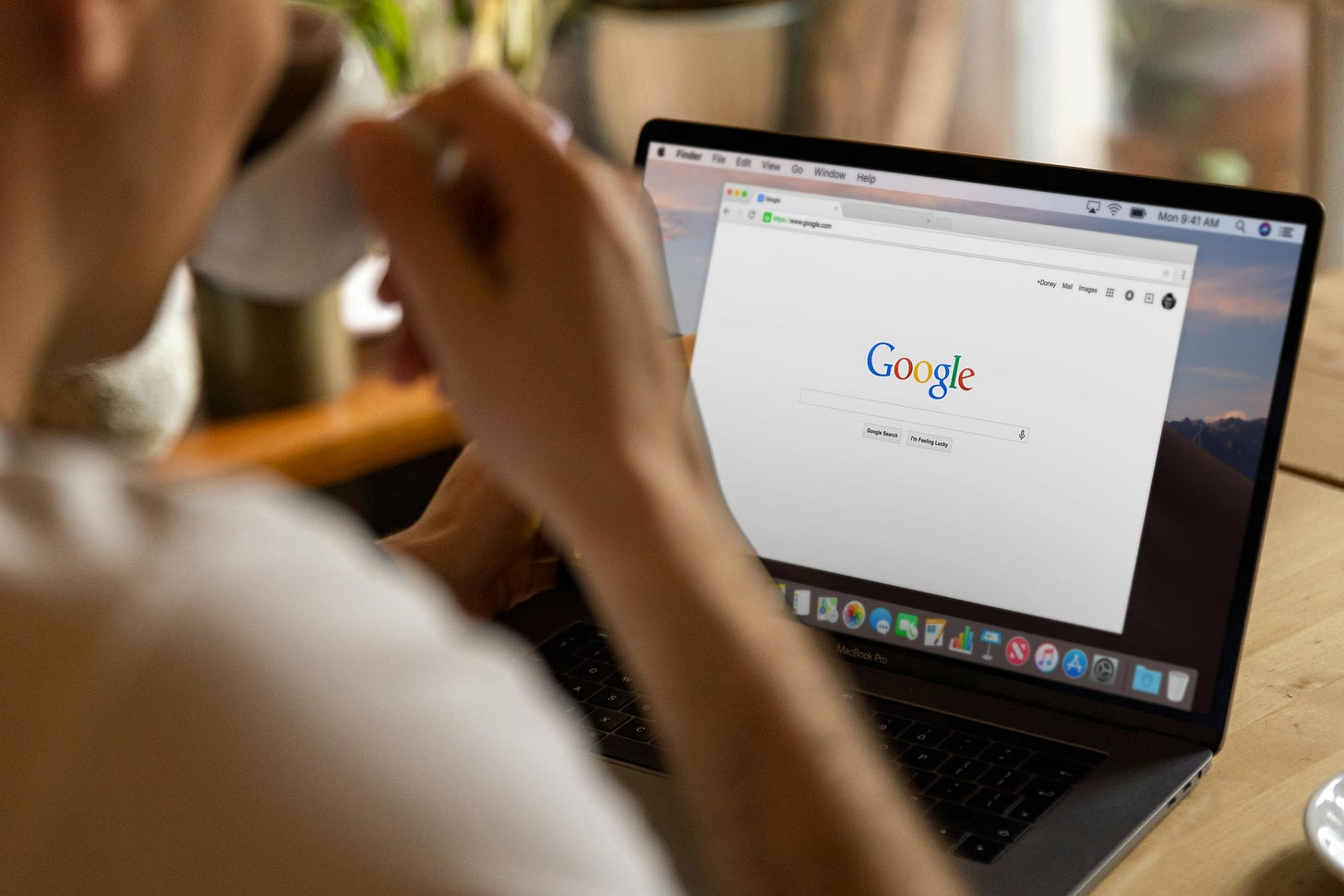 Image shows a person sitting at their desk with a laptop computer showing a browser with Google search engine open.