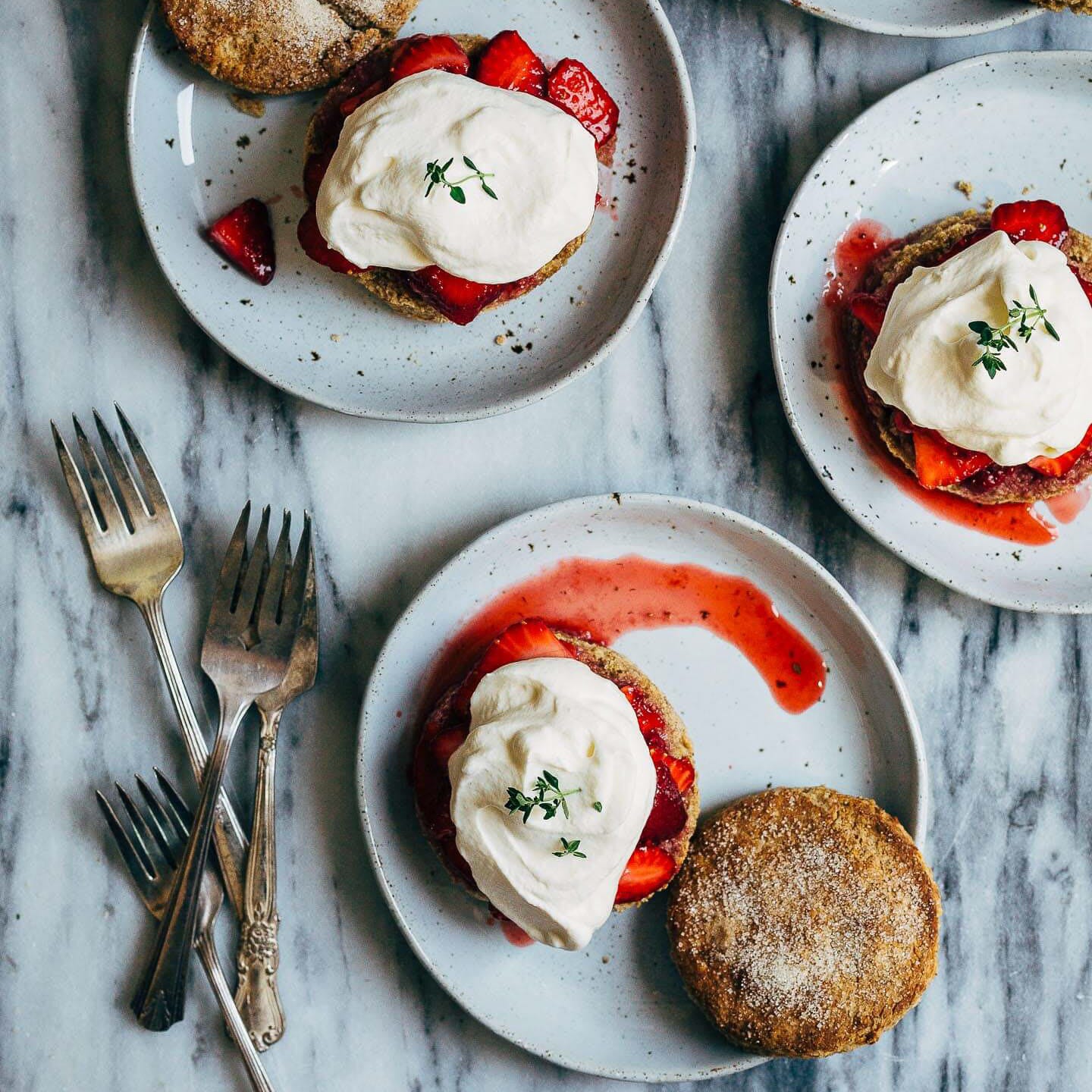 Little plates with whole wheat biscuits, vivid red strawberries, and whipped cream with fresh thyme. 