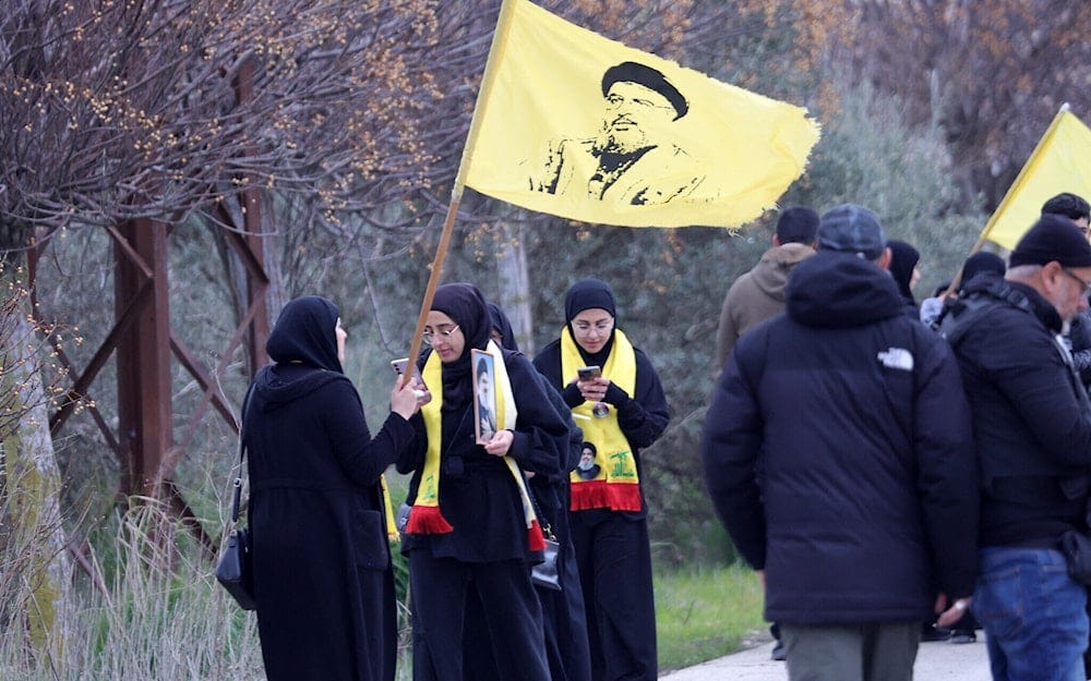 Lebanese women carry a flag and wear scarves bearing an image of martyr leader Sayeed Hassan Nasrallah as they gather in Borj El Mlouk on January 26, 2025, behind an Israeli roadblock across a road leading to their village in southern Lebanon (AFP)