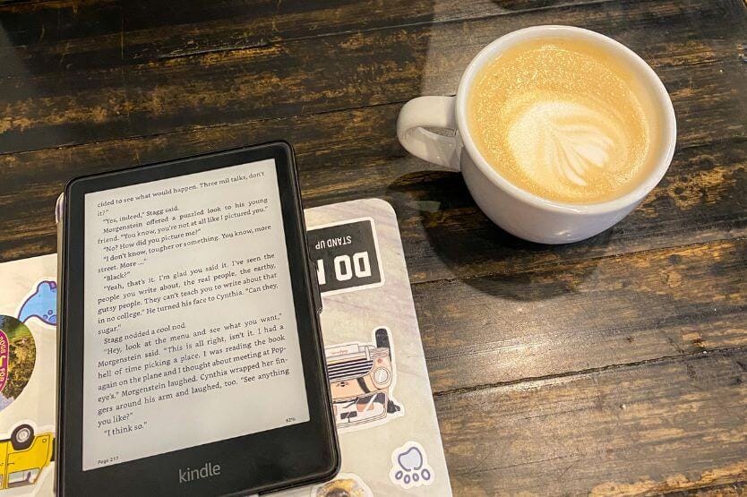 A latte and a Kindle sit on top of a dark wood coffee shop table in a photo taken from above