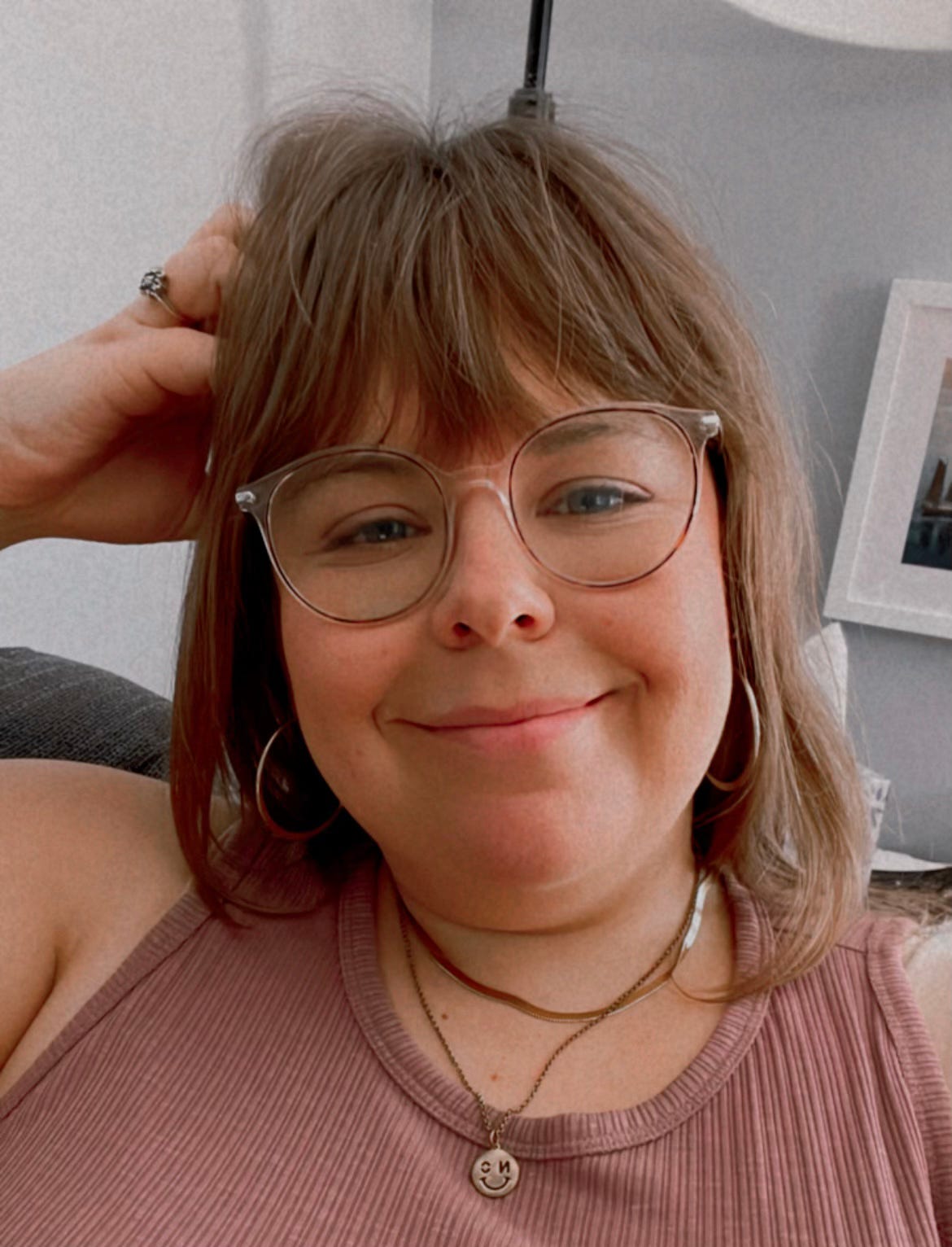 selfie of Melissa who is wearing clear framed glasses, gold jewelry, and a purple tank top