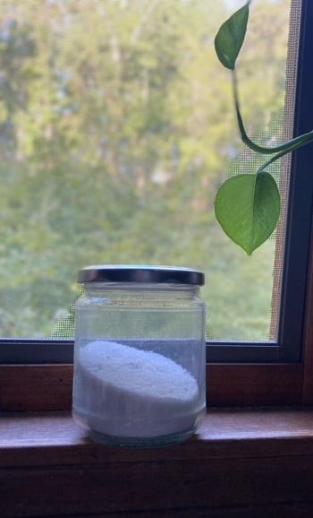 glass container on a window sill filled with a white powder dishwashing detergent