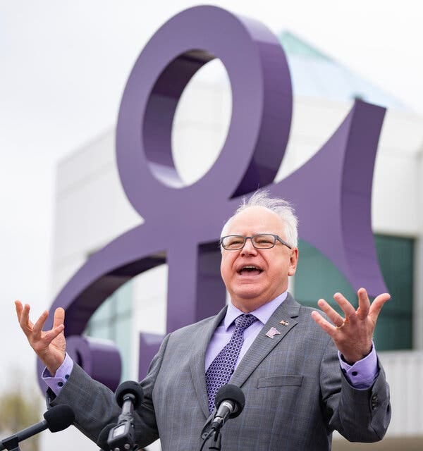 Tim Walz speaks while standing in front of a statue of the musician Prince's love symbol. 