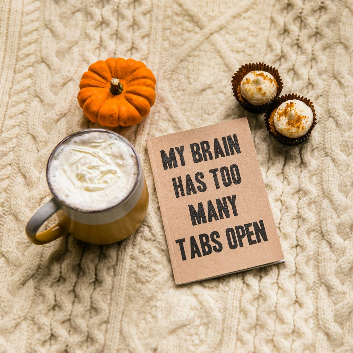 that-s-her-business-KzeOMdcEswk-unsplash.jpg a mug of coffee, a pumpkin, and a fuzzy fall sweater adorn a sign that says, "My brain has too many tabs open."