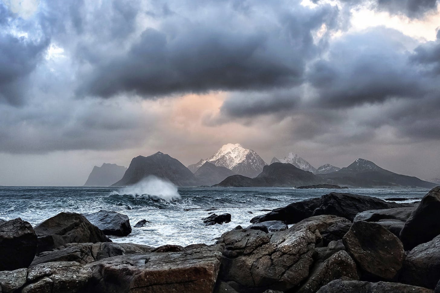 scenic view of snow capped mountains from across the rocky seashore