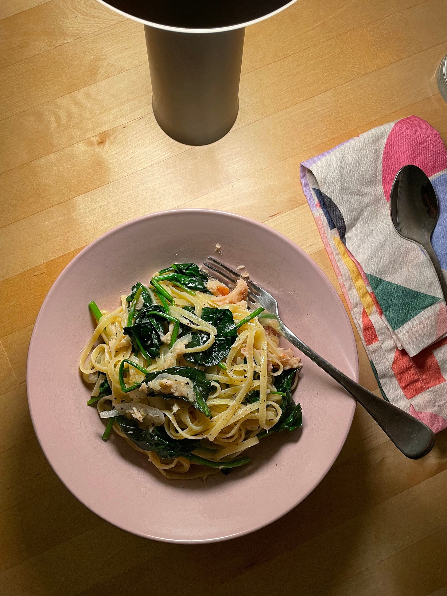 Bowl of linguini on a dining table with chunks of smoked fish and wilted baby spinach.