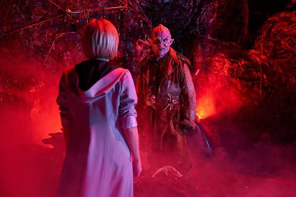 This image shows Ribbons of the Seven Stomachs (played by Kevin Eldon) confronting the Thirteenth Doctor (Jodie Whittaker, back to camera) inside the reddish, hellish anti-zone that connects the Solitract universe to our (primary) reality in "It Takes You Away" (Doctor Who Series 11's ninth episode). This image shows Ribbons of the Seven Stomachs (played by Kevin Eldon) confronting the Thirteenth Doctor (Jodie Whittaker, back to camera) inside the reddish, hellish anti-zone that connects the Solitract universe to our (primary) reality in "It Takes You Away" (Doctor Who Series 11's ninth episode).