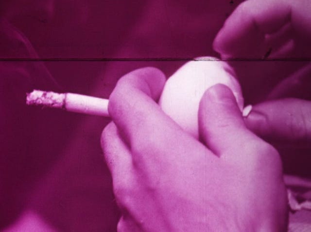 Movie still from Hollis Frampton's Process Red. A hand holding a cigarette, peeling an egg, overlaid in violet