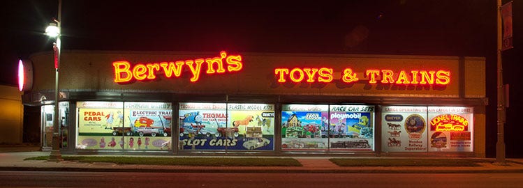 Night photo of toy store with Berwyn's Toys and Trains in fluorescent orange lettering.