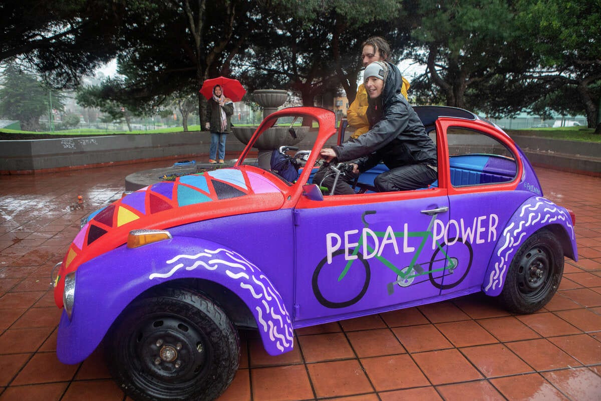Deborah Gutof (front) drives a bike car created by Eric Schmidt (left) out of the shell of a 1971 VW Beetle named "Pedal Power" at Potrero del Sol Park in San Francisco on Jan. 11, 2023. The vehicle is powered by human power from two bicycles mounted inside the vehicle.