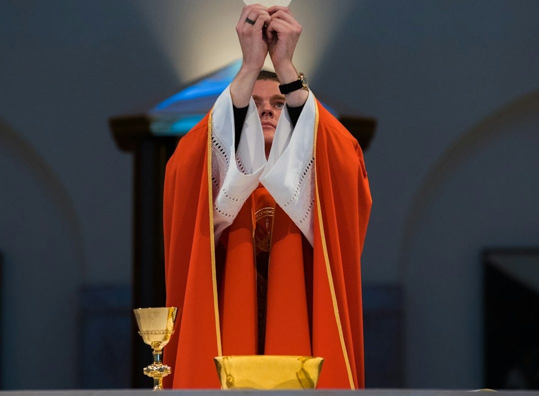 A priest in a red robe offering communion in front of an altar in Kingwood