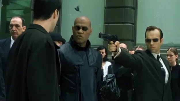 Screenshot from The Matrix (1999). Morpheus says to Neo "look again" and the simulated person he saw a moment ago has now turned into Smith, an agent of the enemy.